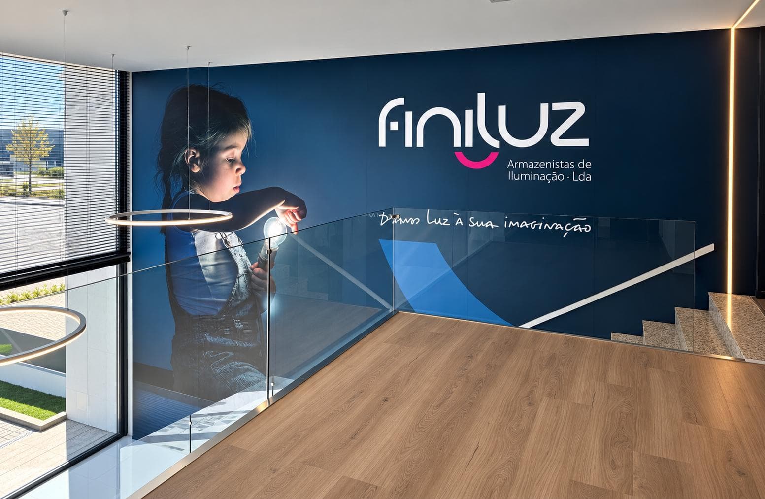 Mezanino com mural de uma criança com uma lâmpada, o logótipo Finiluz e a frase "Damos luz à sua imaginação", atrás de um guarda de vidro